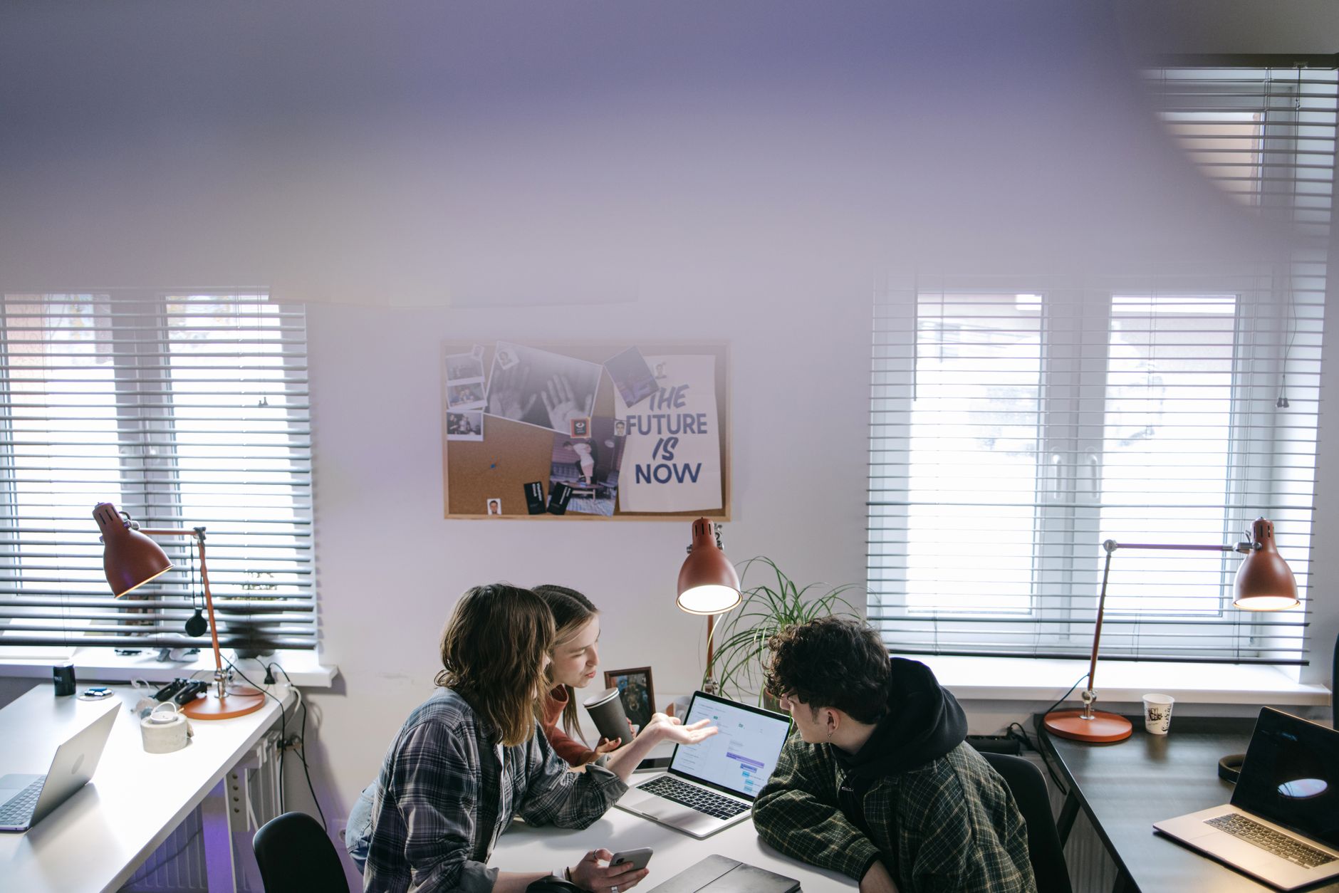 A group of people discussing ideas around laptops in a bright, modern office space — illustrating: Virtual SOC vs In-House Security Teams: Which Model Fits Your Central Florida SMB?